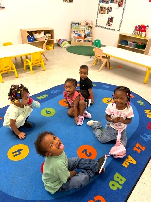 Children sitting together on an alphabet rug in the classroom