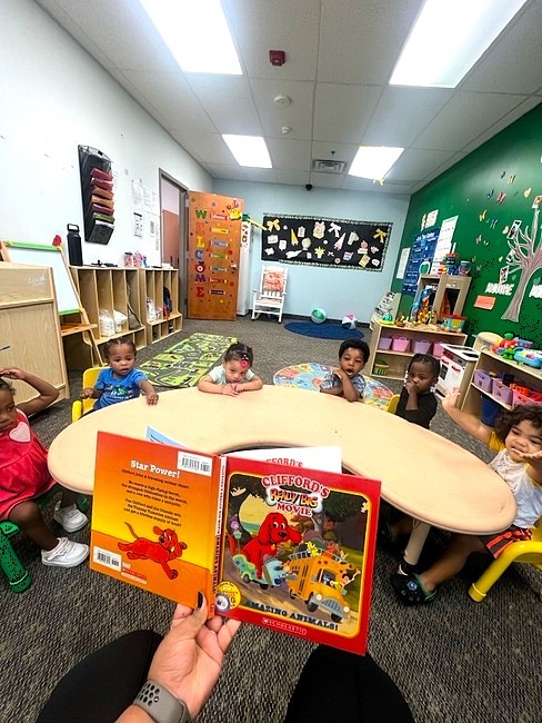 A teacher reading a picture book to children seated at a round table