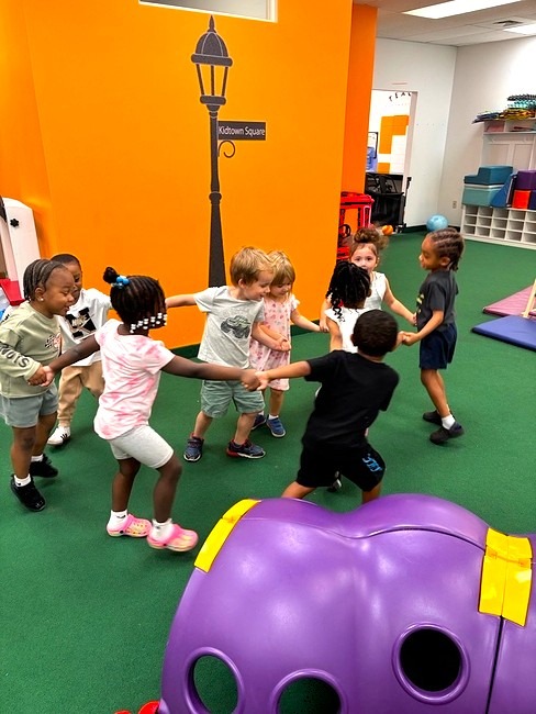 Toddlers holding hands in a circle on the classroom carpet