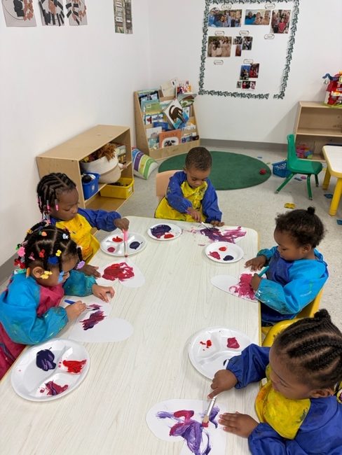 Toddlers in smocks painting with purple and red paint