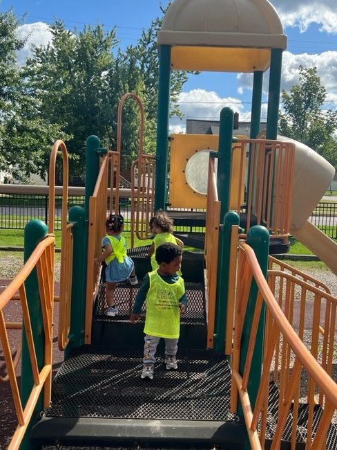 Toddlers in safety vests climbing the playground steps
